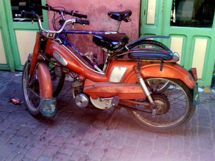 滑板车——一辆摩托车和一辆自行车停在露天市场的墙上——独自前往摩洛哥马拉喀什