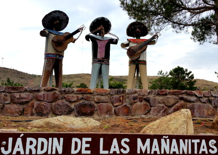 三个金属乐队在德克萨斯州阿尔卑斯的贝恩斯公园演奏音乐，雕塑下面用白色漆着“马纳尼塔斯花园”的字样