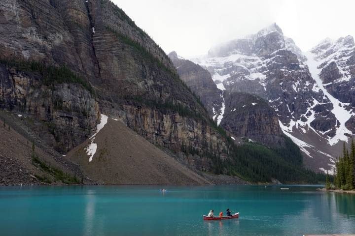 在加拿大阿尔伯塔省班夫国家公园被群山环绕的蓝绿色冰碛湖上划独木舟