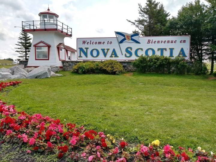 这个小的灯塔复制品旁边的欢迎来到新斯科舍省的标志迎接旅客从加拿大新不伦瑞克省进入新斯科舍省