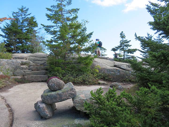 巨大的石碑路标和两个徒步旅行者站在树旁的一块大石头上。