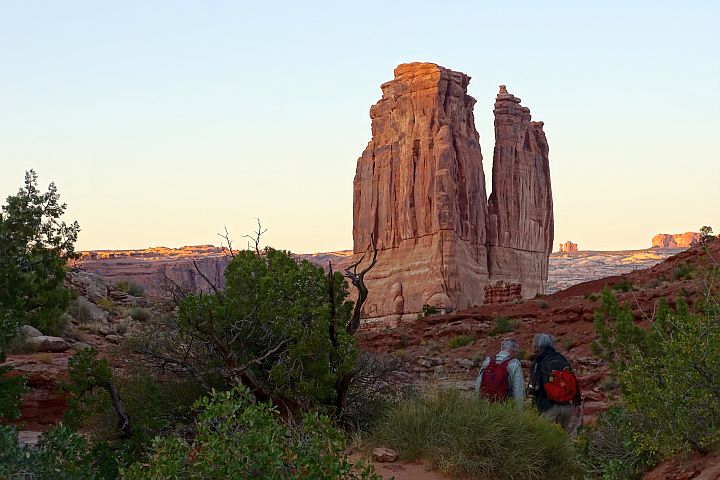 前景中的两名徒步旅行者正走向巨大的塔状岩层，即法院塔。