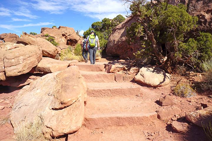 两名徒步旅行者走上天然石阶，石阶旁有巨石和杜松树。
